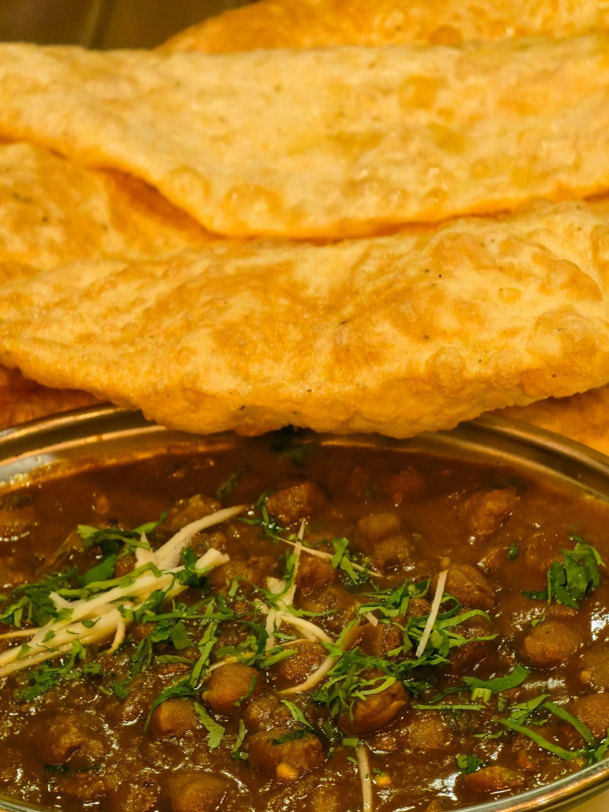 Chole garnished with ginger and coriander beside a puffed bhatura