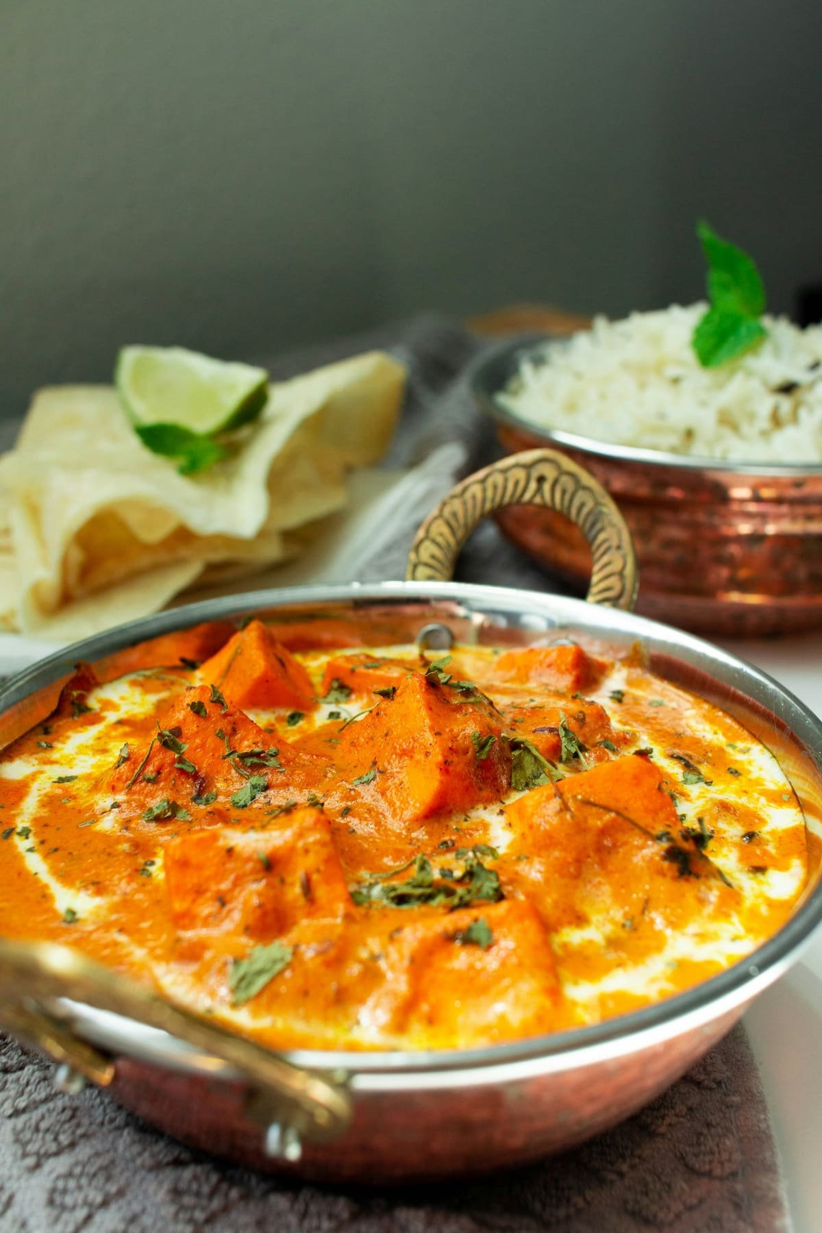 Paneer butter masala in a copper bowl with rice and papad
